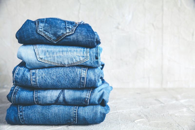 stack of blue jeans on a gray background | JeansFix